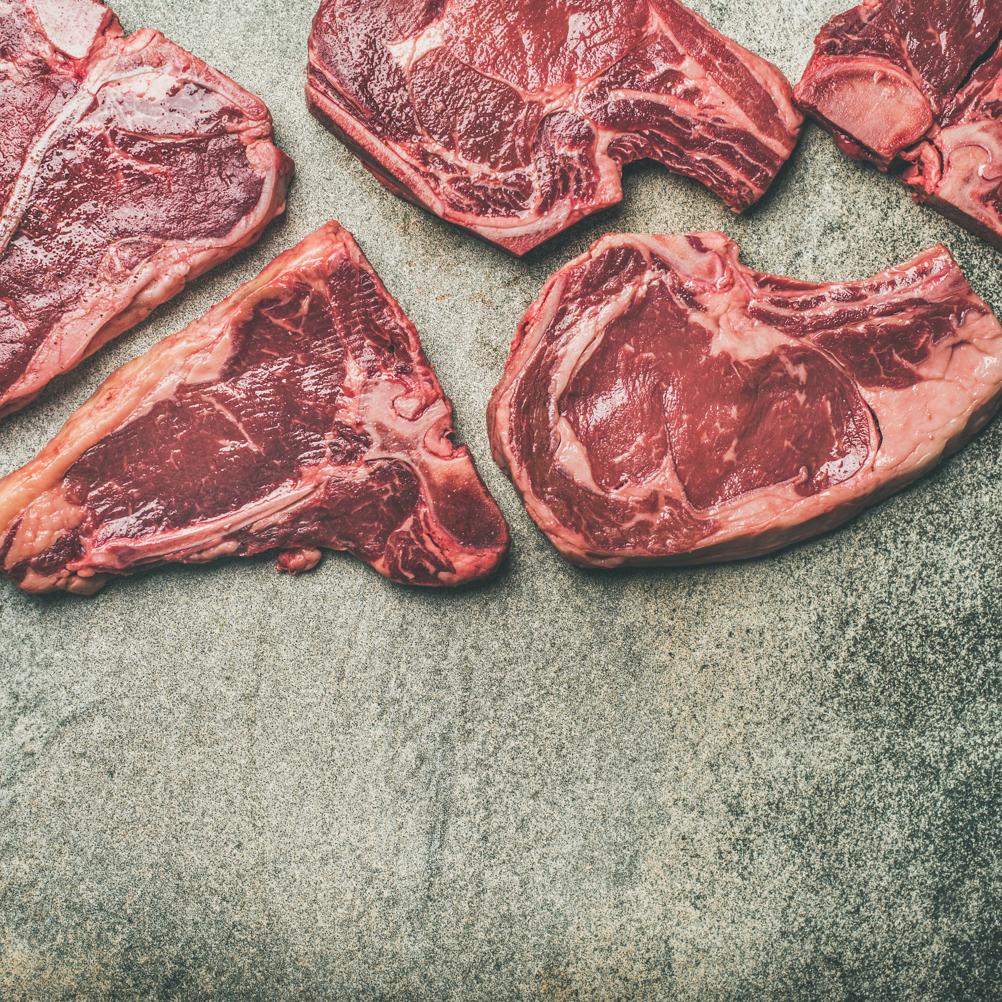 Porterhouse, t-bone and rib-eye steaks over grey background, square crop